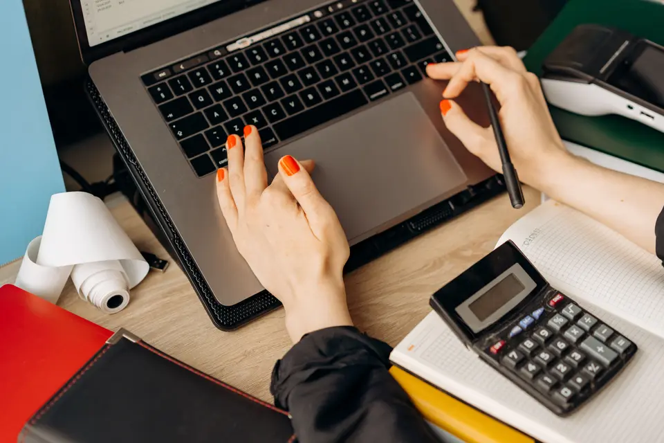 A bookkeeper at a desk working through paperwork beside a laptop
