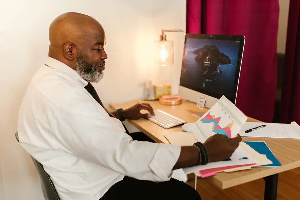 A finance professional at a desk reviewing a printed chart beside a computer