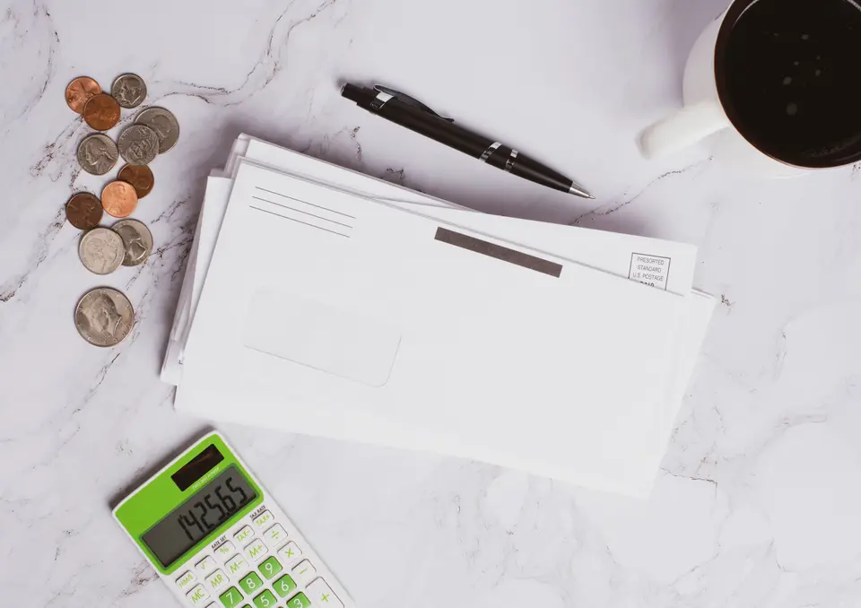 A stack of window envelopes, coins and a calculator on a marble desk